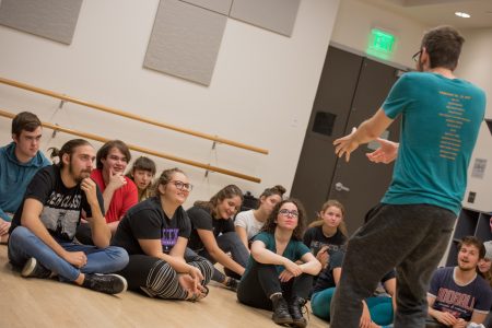 Students sit on the floor and look up at the teacher in a comedy class