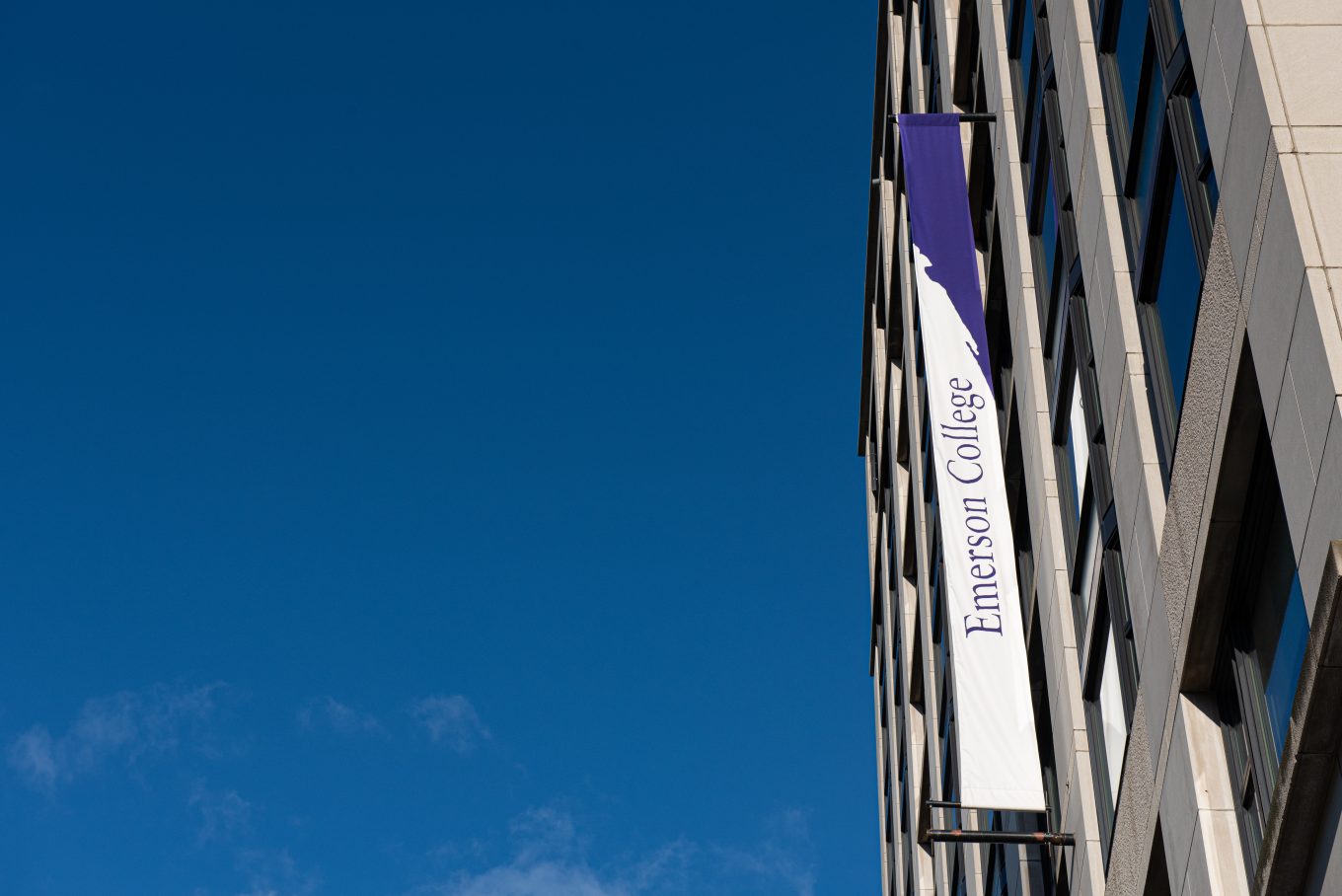 shot of Emerson College building with purple and white banners against a blue sky