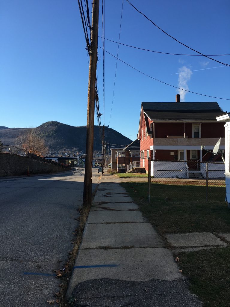 An empty road in New Hampshire, a sidewalk, and a house, with mountains in the background