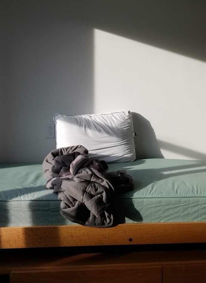 An empty bed with a blanket and pillow on it in a dorm room