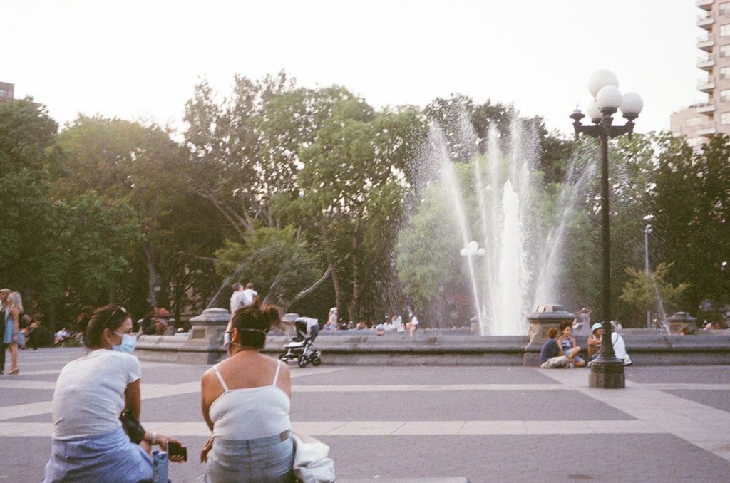 Two women sitting next to each other on a bench looking at a fountain in Washington Square Park in NYC