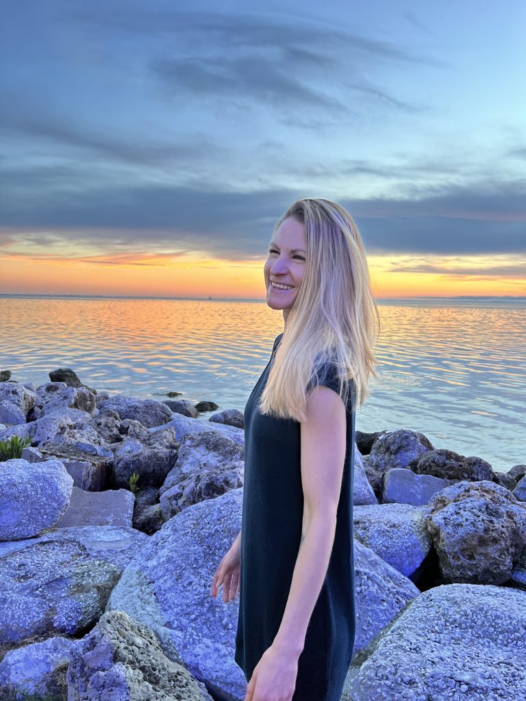 Whitney Phillips smiles by the ocean with the sun setting