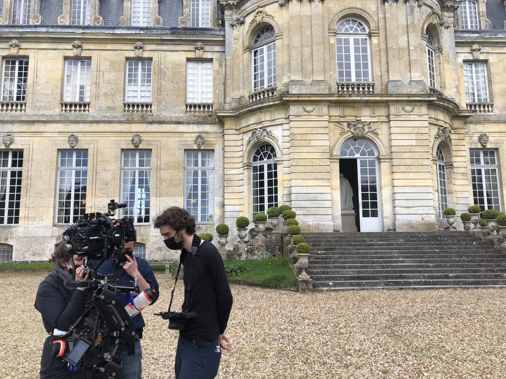Three students confer on a film shoot outside of a chateau by Paris