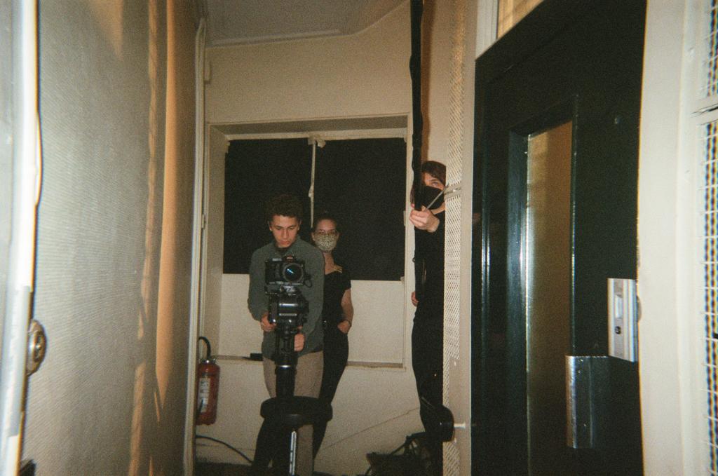 A person stands at the end of a hallway with a film camera ready to roll for action