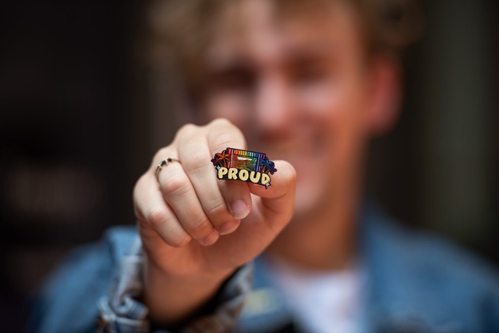 Someone holds a rainbow colored ring that says proud