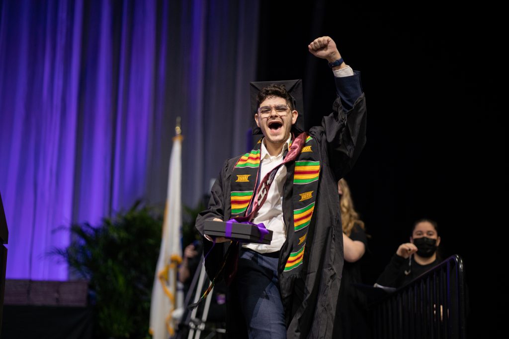 An alum cheers after receiving his diploma