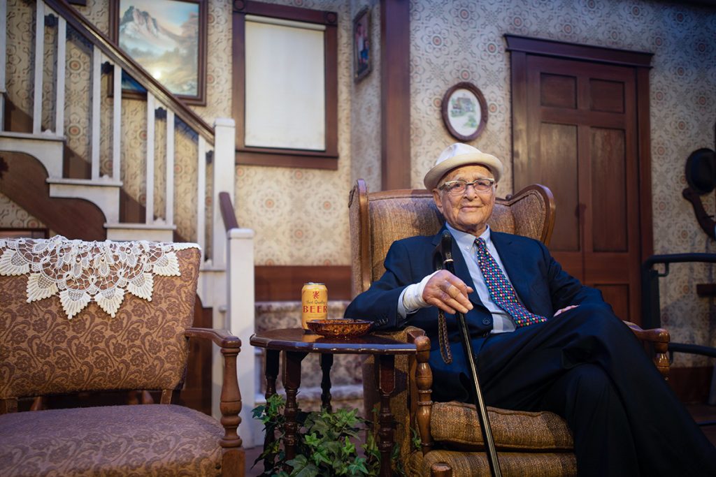Lear sits in a replica of the All in the Family set