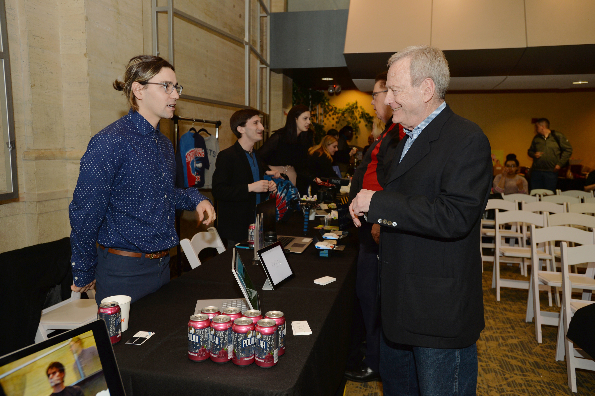 Students and faculty discuss business ideas in the Emerson E3 expo, around tables with information and presentations.