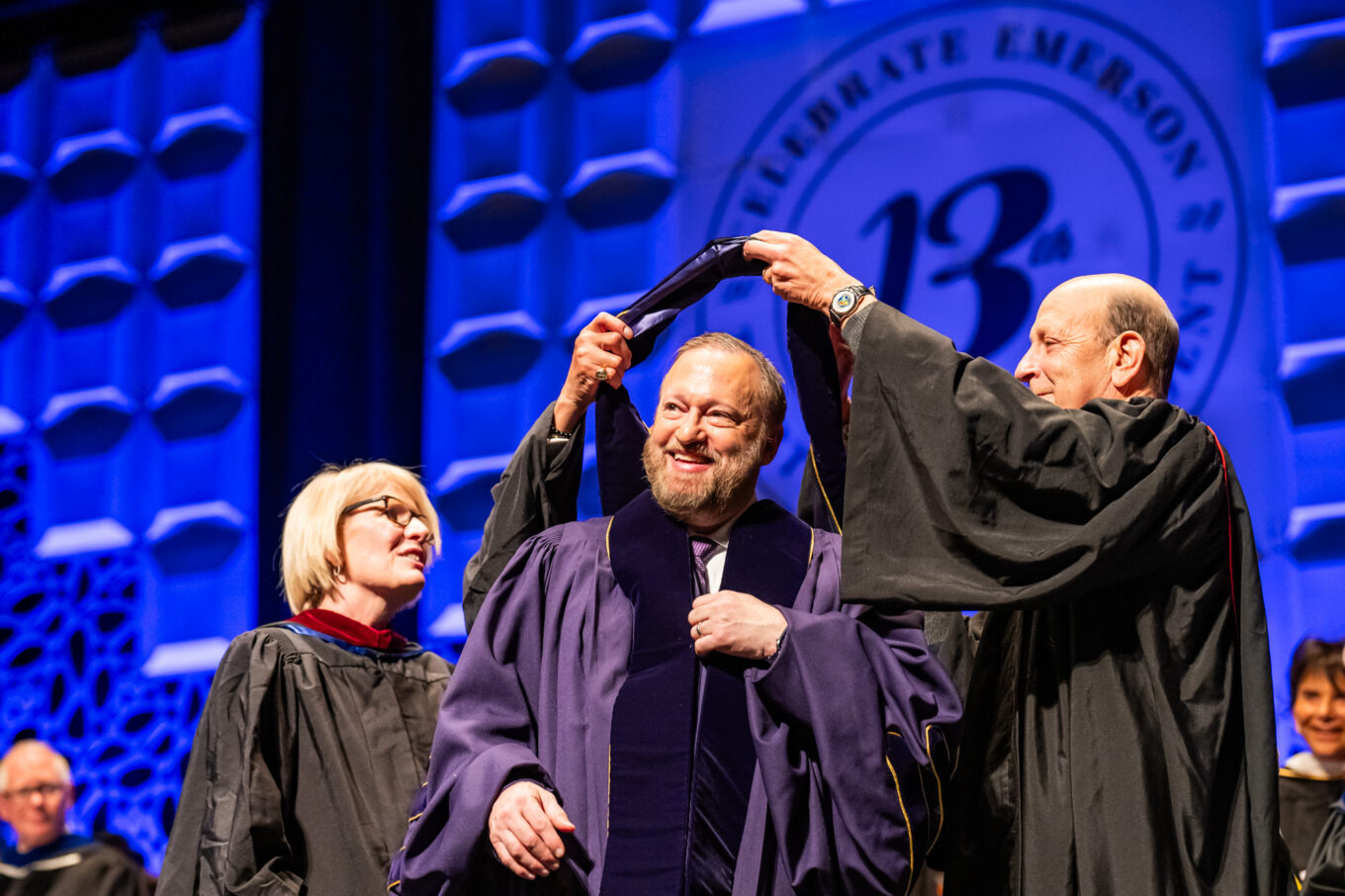 Trustees Ellen Calmas and Robert Miller help President Bernhardt put on his new Emerson regalia and hood.