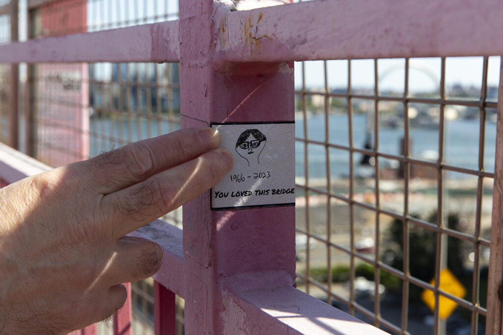 A closeup of two fingers pointing to a sticker on a footbridge 